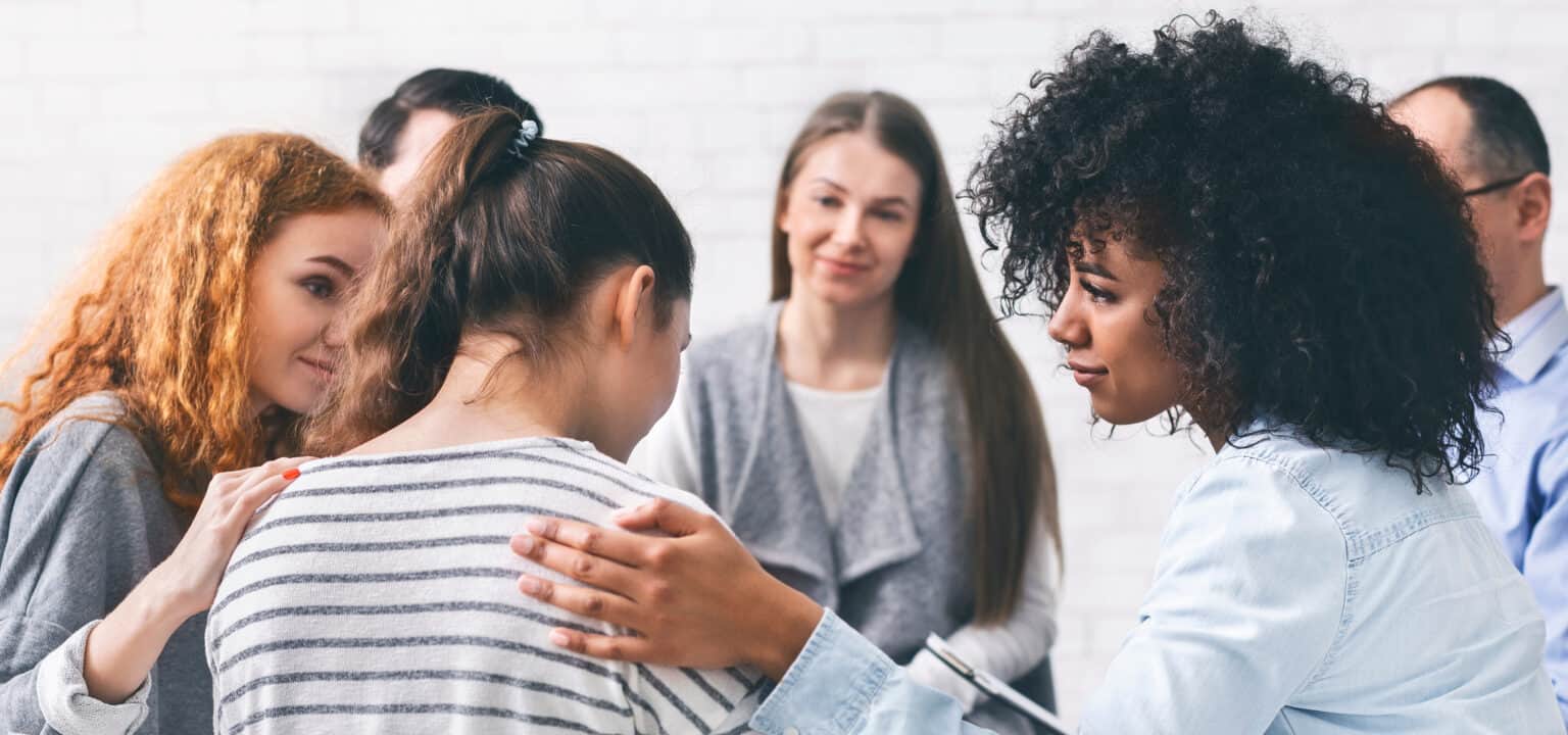 Supportive group therapy session with diverse individuals encouraging a friend in recovery.