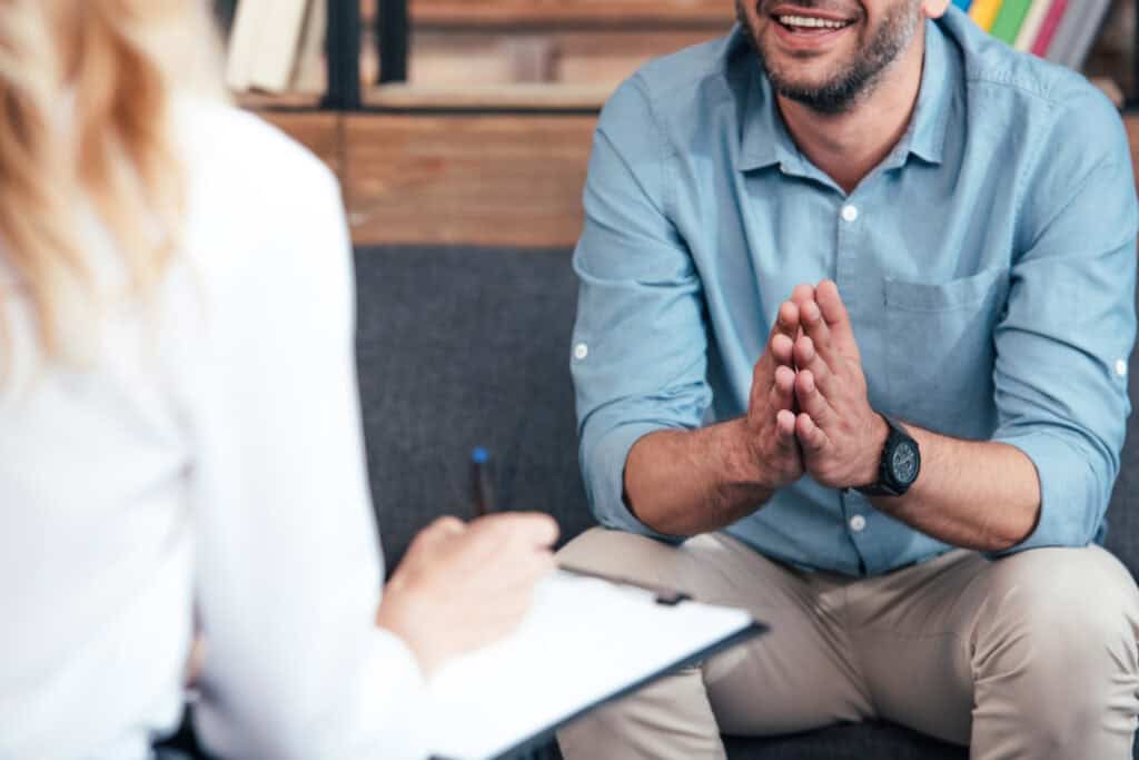 Therapist in a counseling session with a client, hands clasped in a calm, attentive pose.