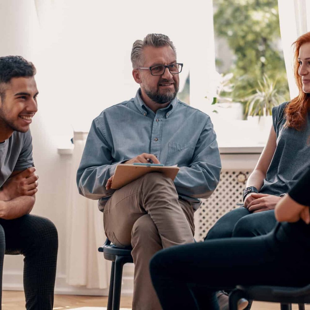 Smiling spanish man talking with friends during meeting for teenagers with therapist